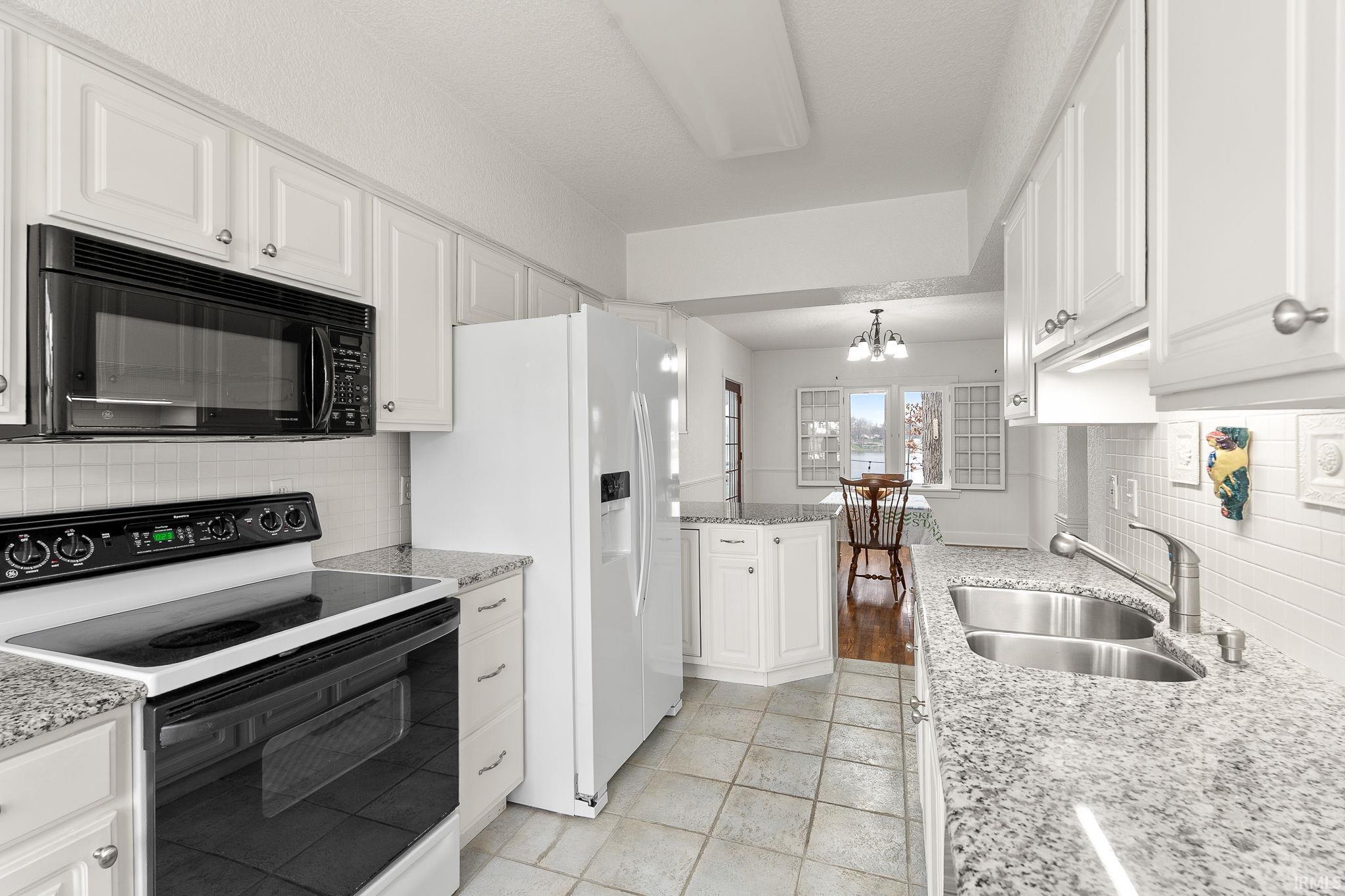 Kitchen with range with electric cooktop, light stone countertops, backsplash, black microwave, and white cabinetry