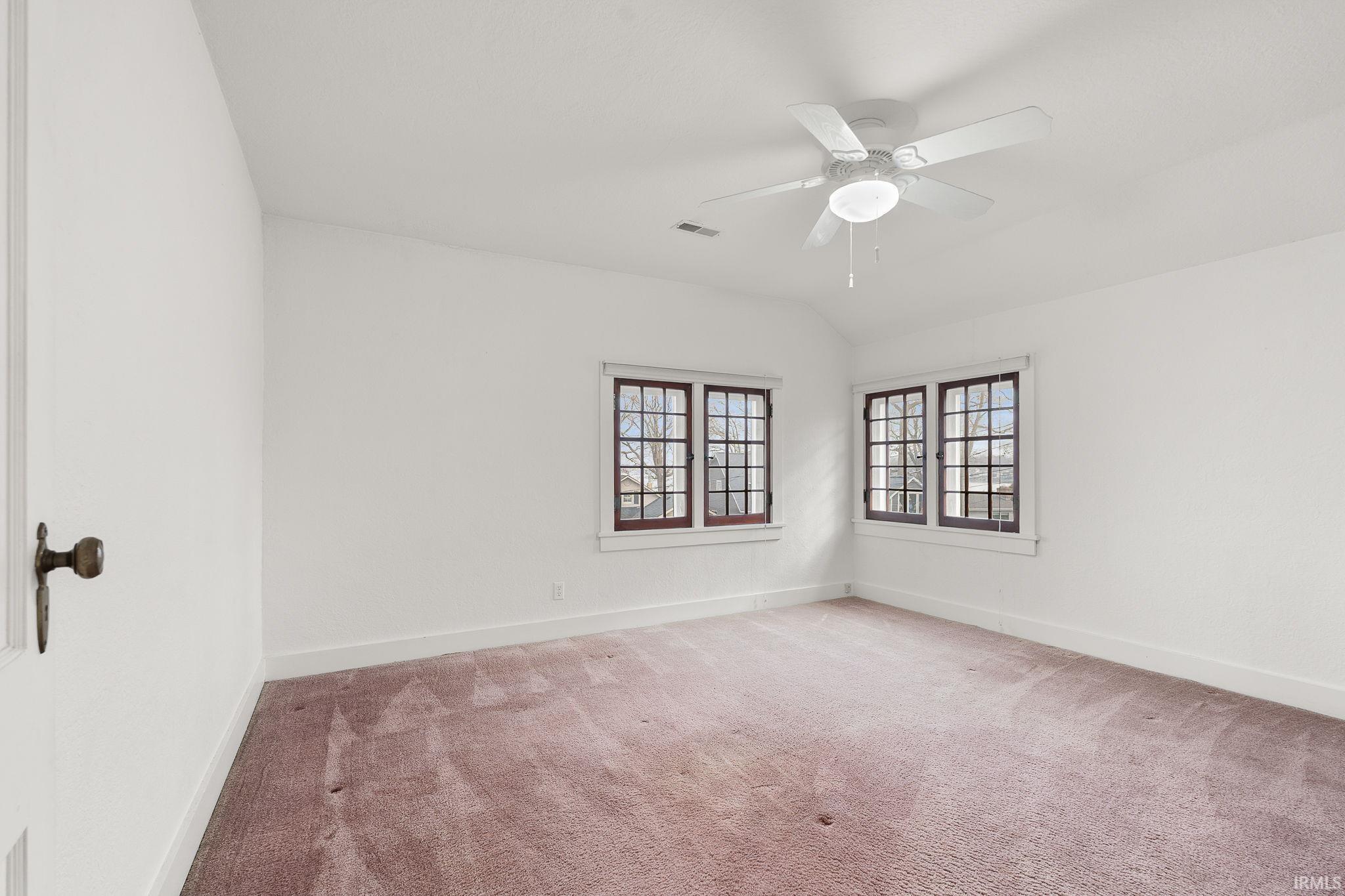 Spare room featuring light colored carpet, lofted ceiling, and ceiling fan