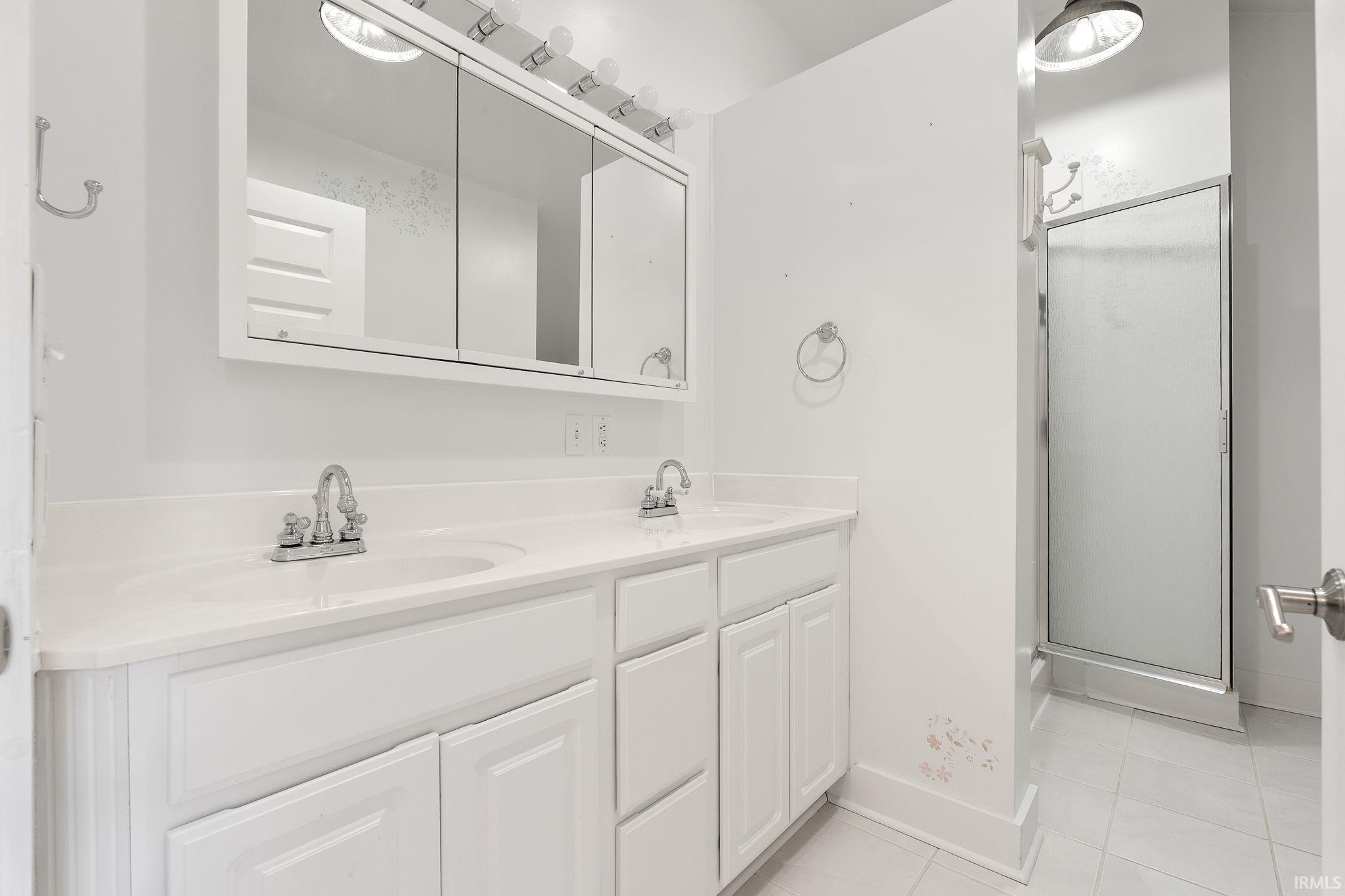Bathroom featuring double vanity, a shower stall, and light tile patterned floors