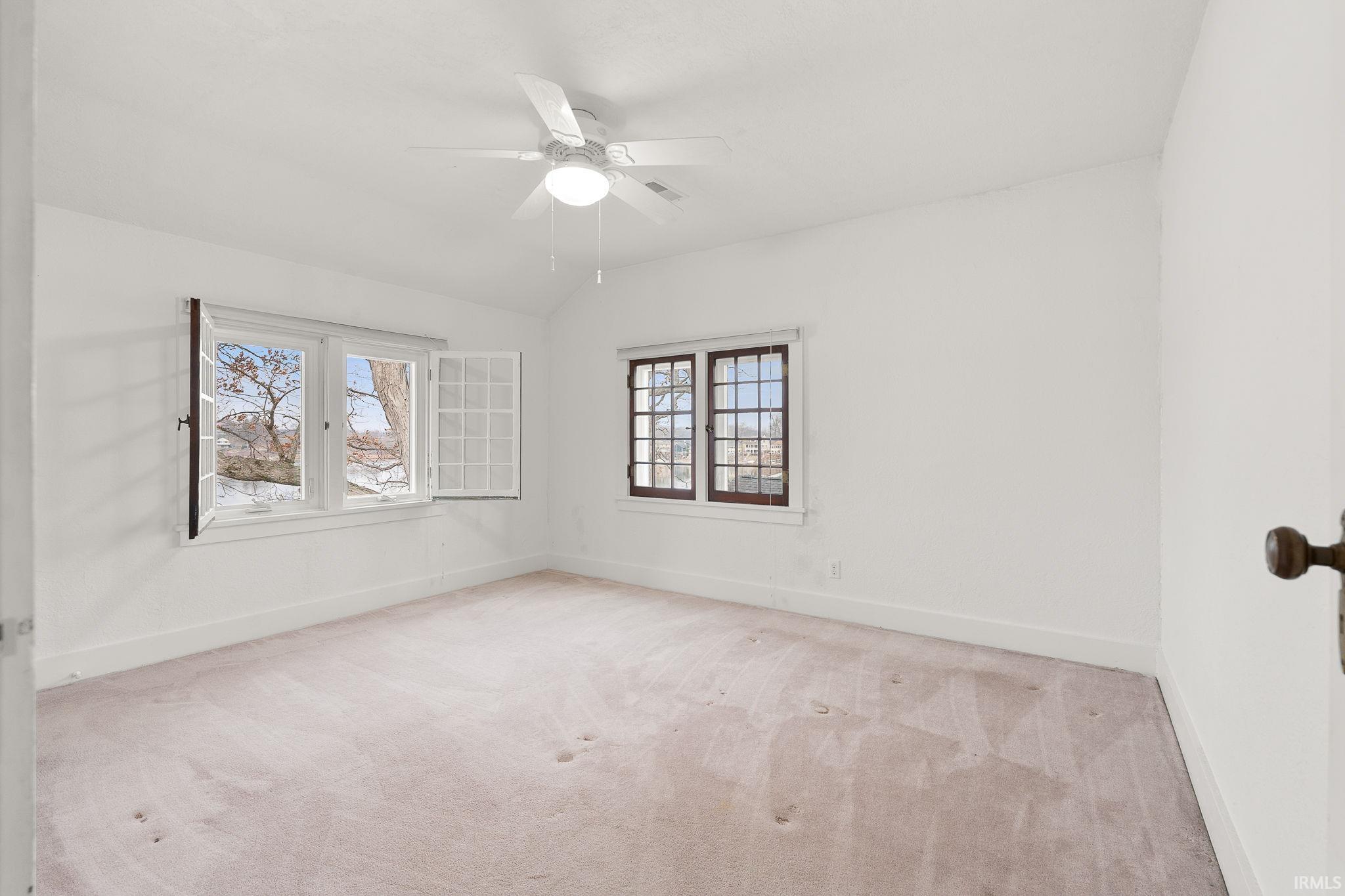 Empty room with light carpet, vaulted ceiling, and ceiling fan