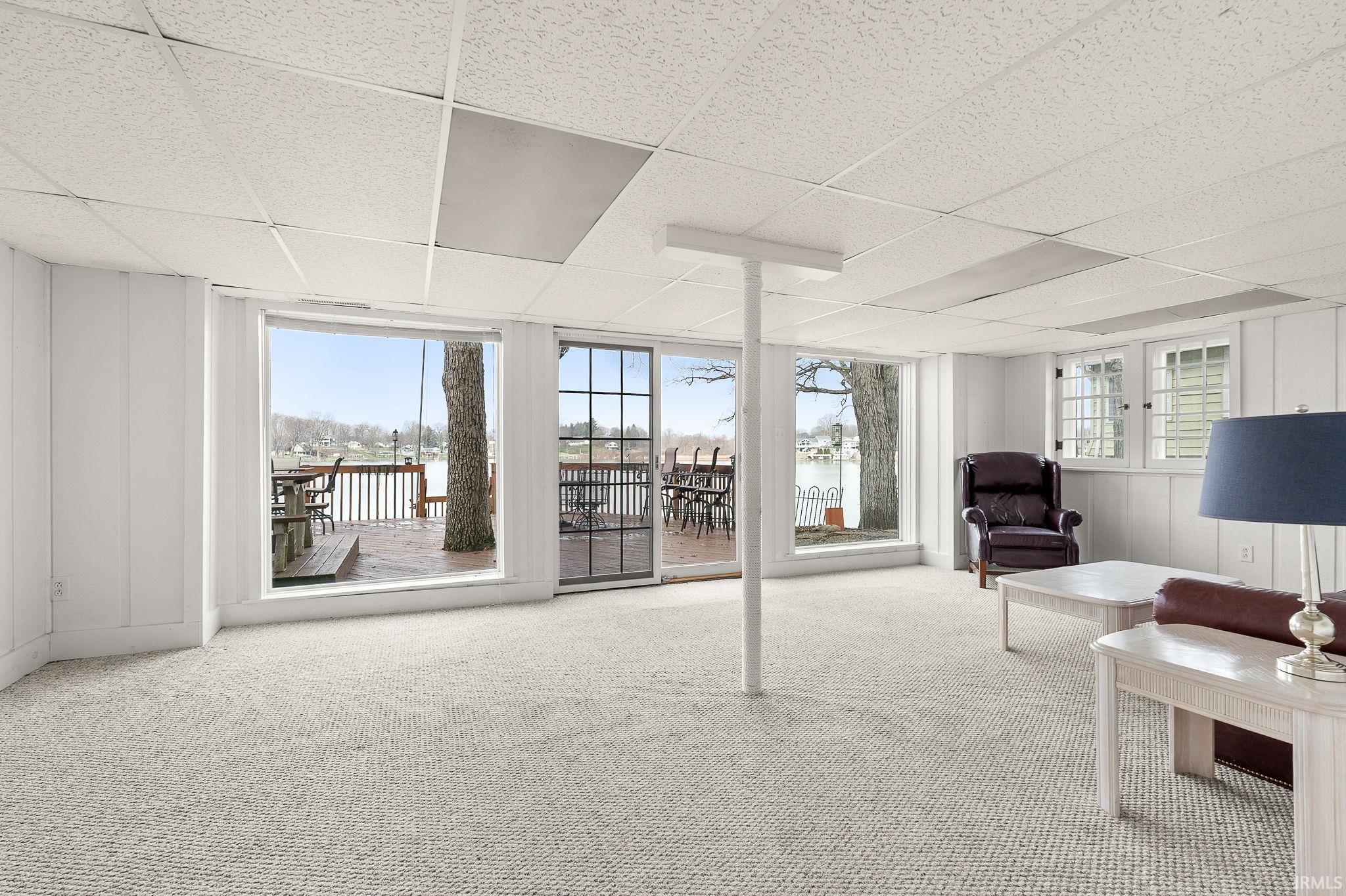 Carpeted living room with a drop ceiling, plenty of natural light, and a decorative wall
