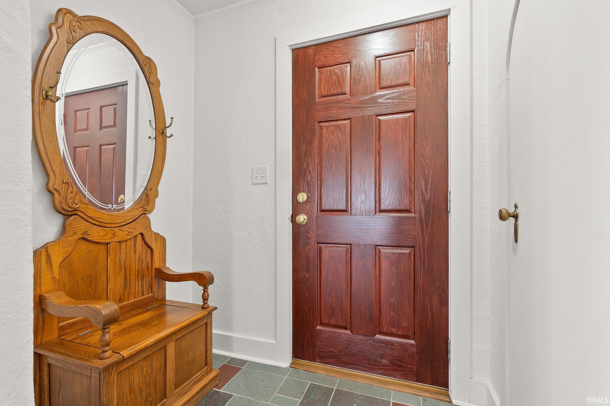 Foyer entrance with crown molding, dark tile patterned flooring, and a textured wall