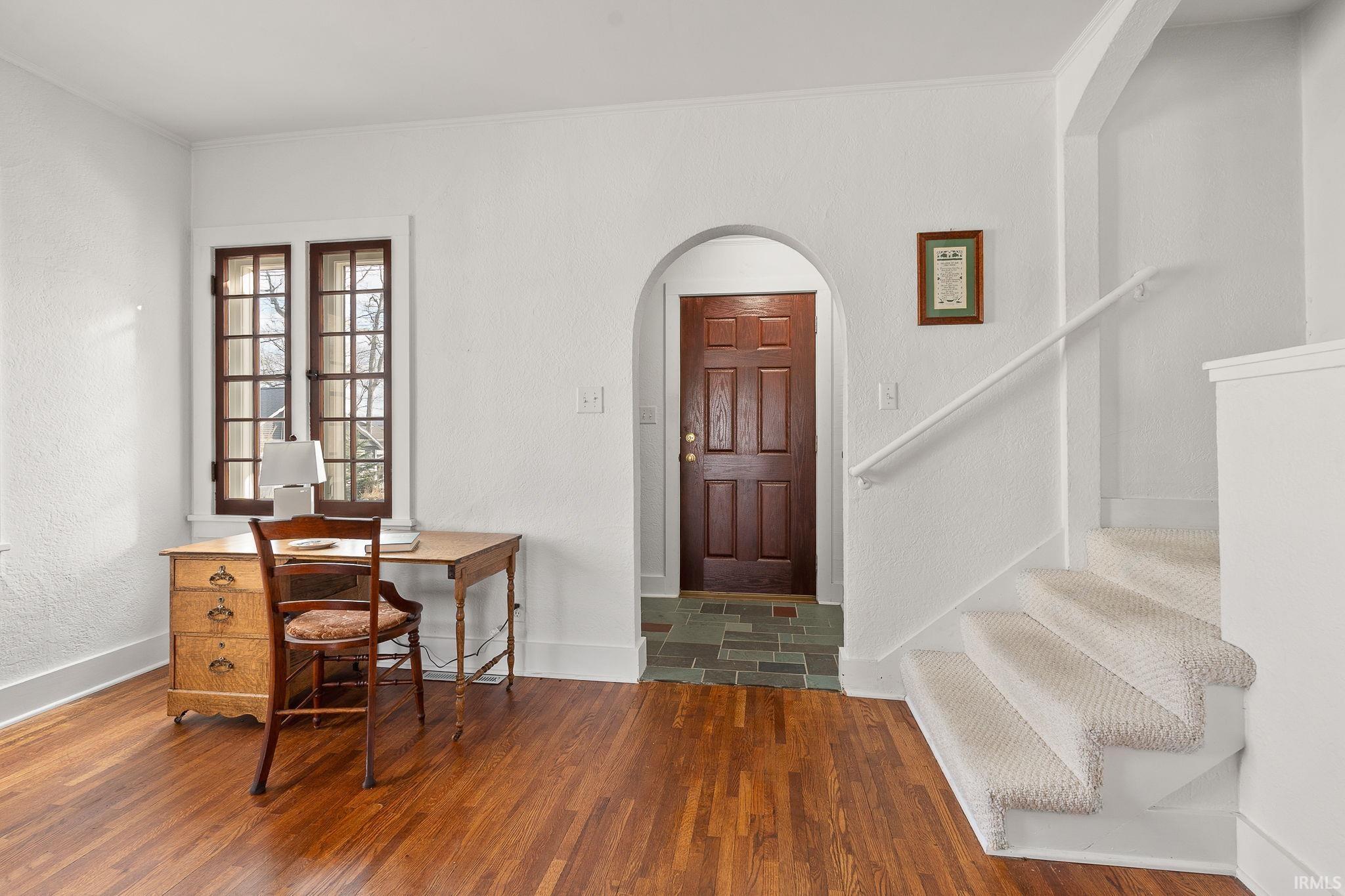Foyer entrance featuring arched walkways, crown molding, a textured wall, and wood finished floors