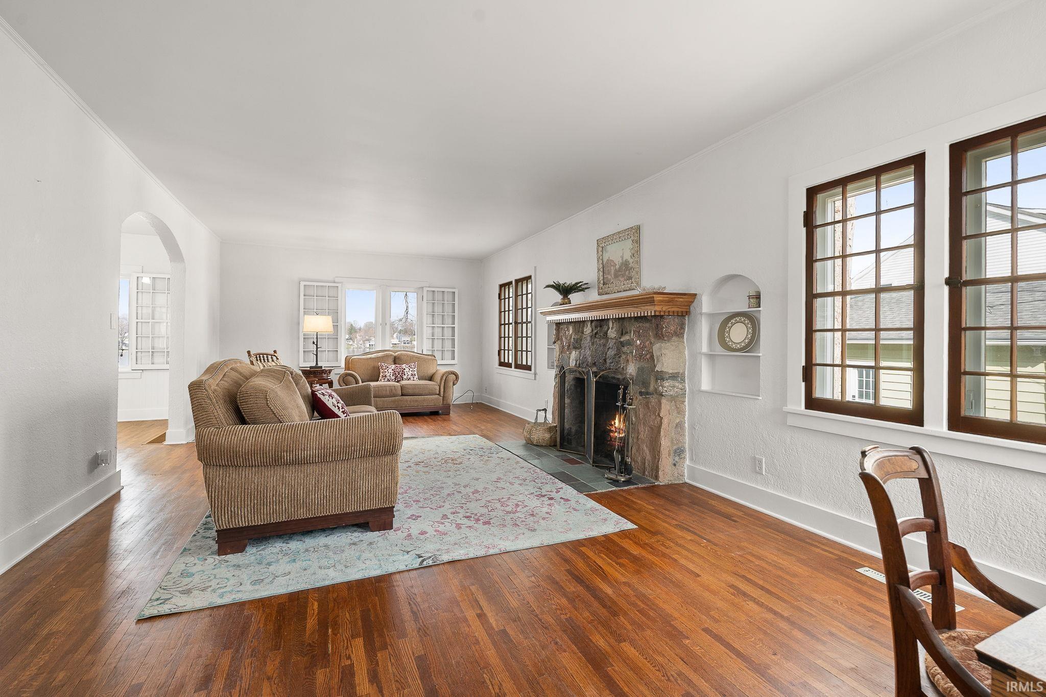 Living room featuring arched walkways, a fireplace with flush hearth, hardwood / wood-style flooring, and crown molding