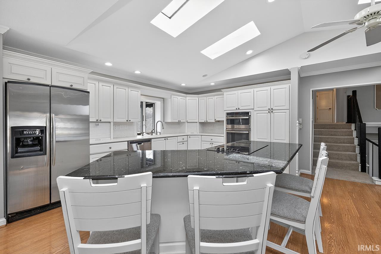 Kitchen with stainless steel appliances, white cabinets, light wood-style floors, dark stone countertops, and vaulted ceiling