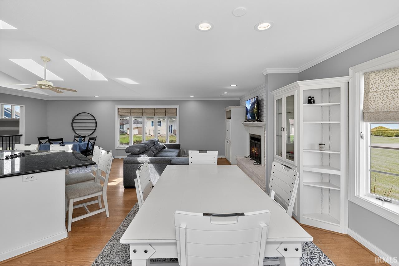 Dining room with a warm lit fireplace, a skylight, light wood-style flooring, ornamental molding, and ceiling fan