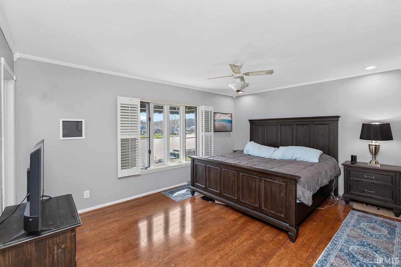 Bedroom with dark wood-style flooring, a ceiling fan, and crown molding