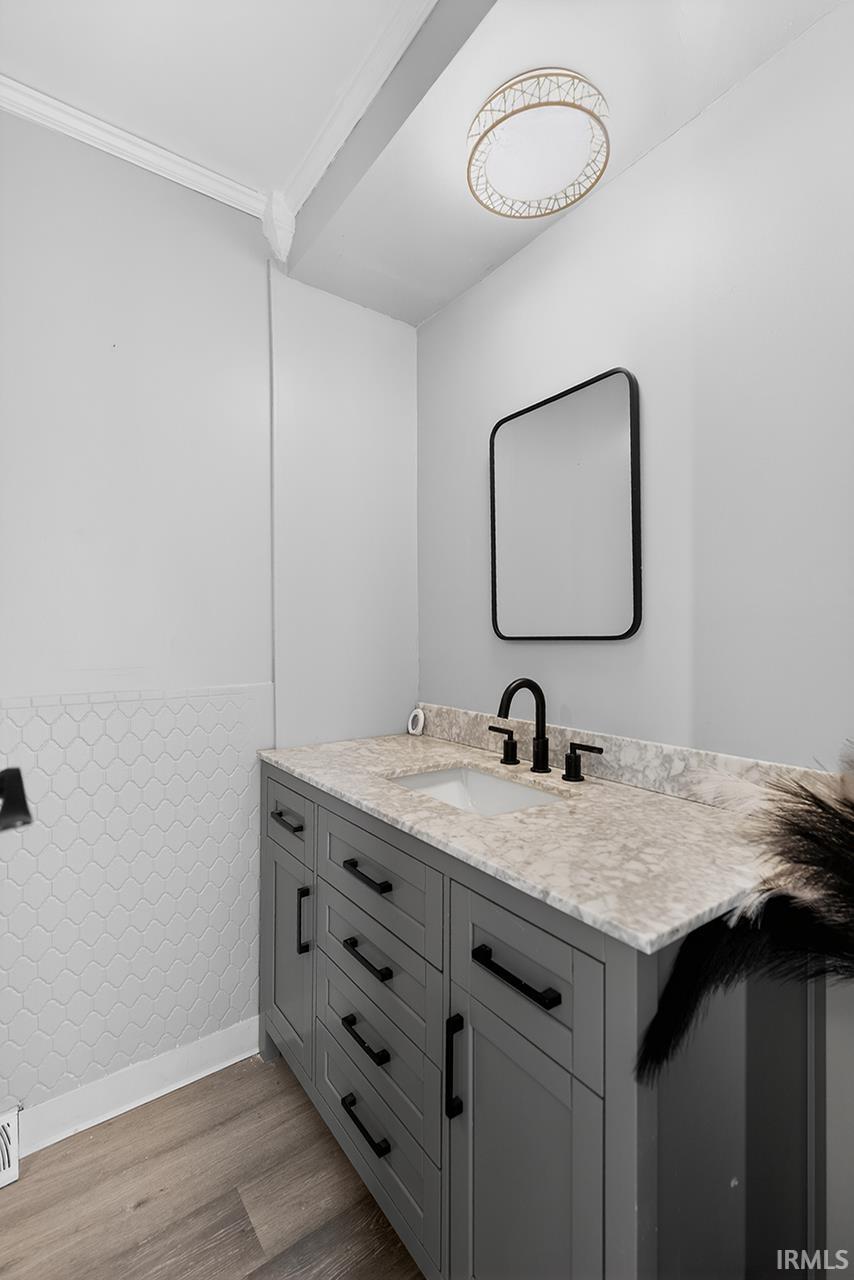 Bathroom featuring vanity, light wood-style flooring, a wainscoted wall, and crown molding