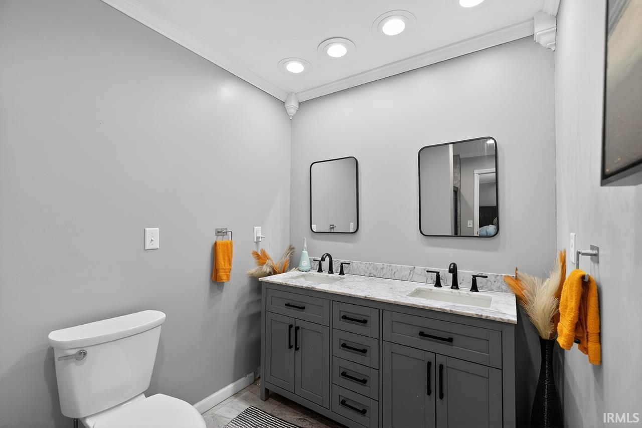 Full bathroom featuring double vanity, ornamental molding, and light marble finish flooring