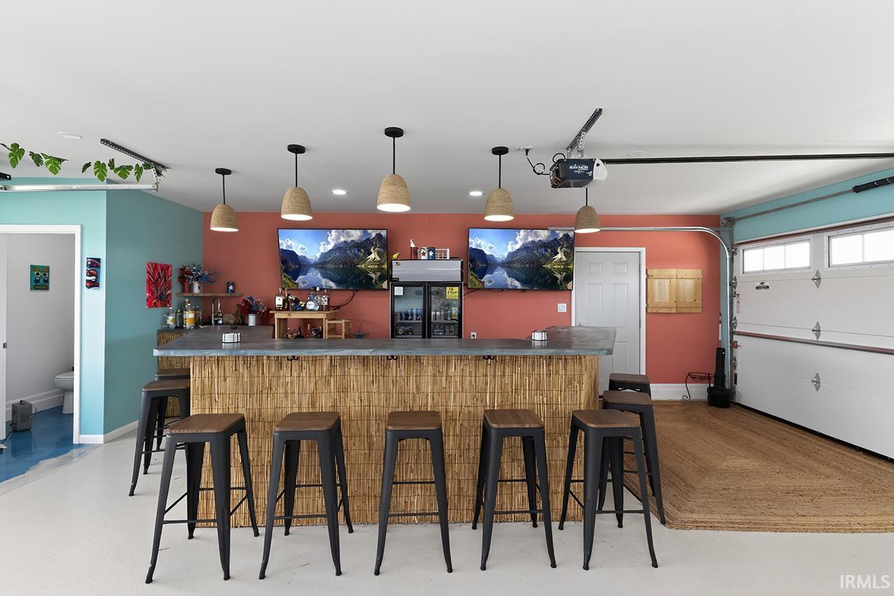 Indoor bar featuring finished concrete floors, dark countertops, and hanging light fixtures