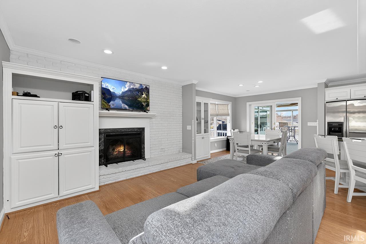 Living room with ornamental molding, light wood-style floors, a brick fireplace, and recessed lighting