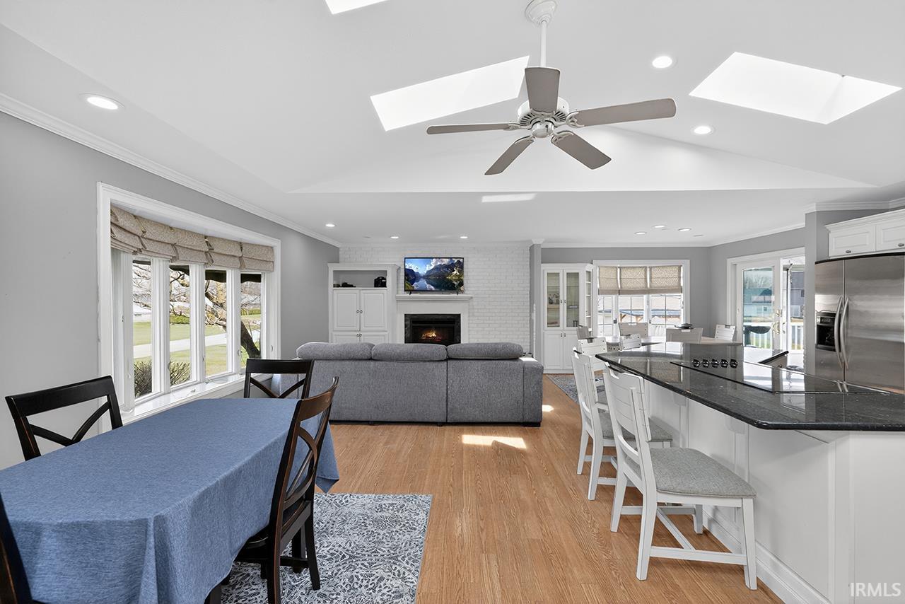 Dining room featuring crown molding, a skylight, a large fireplace, light wood finished floors, and recessed lighting