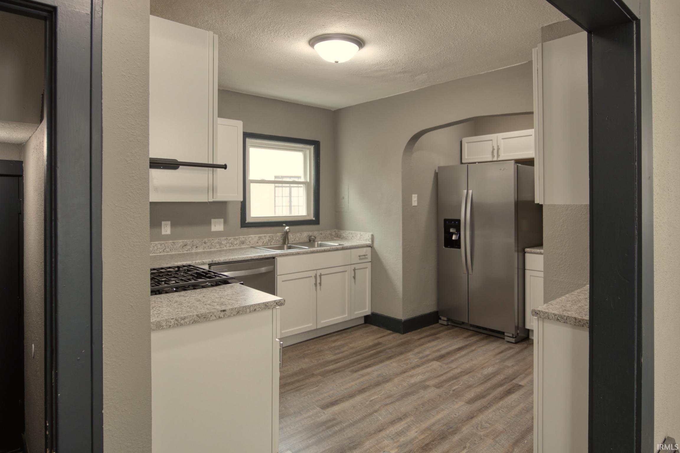 Kitchen featuring a textured ceiling, stainless steel appliances, light countertops, white cabinets, and arched walkways
