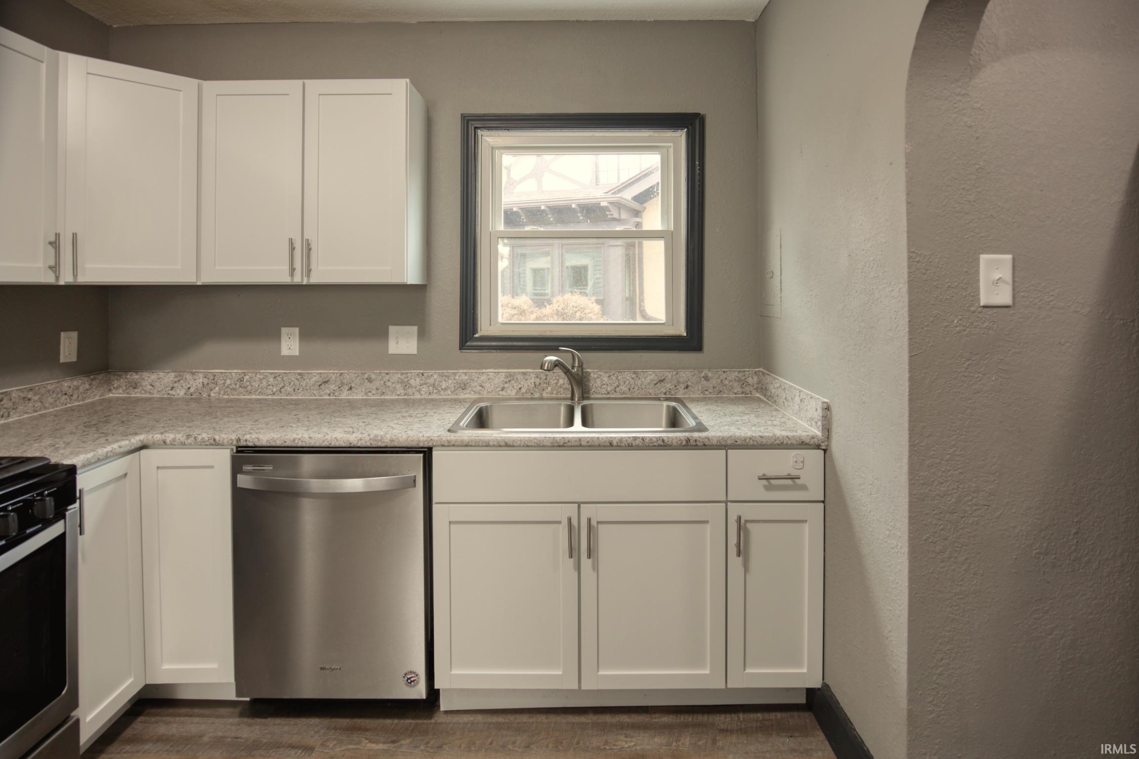 Kitchen featuring white cabinetry, stainless steel appliances, light countertops, a textured wall, and dark wood-type flooring