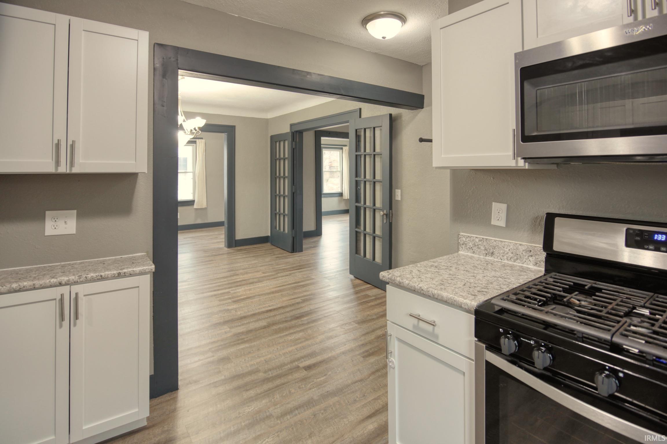 Kitchen featuring appliances with stainless steel finishes, white cabinetry, a chandelier, and light wood finished floors