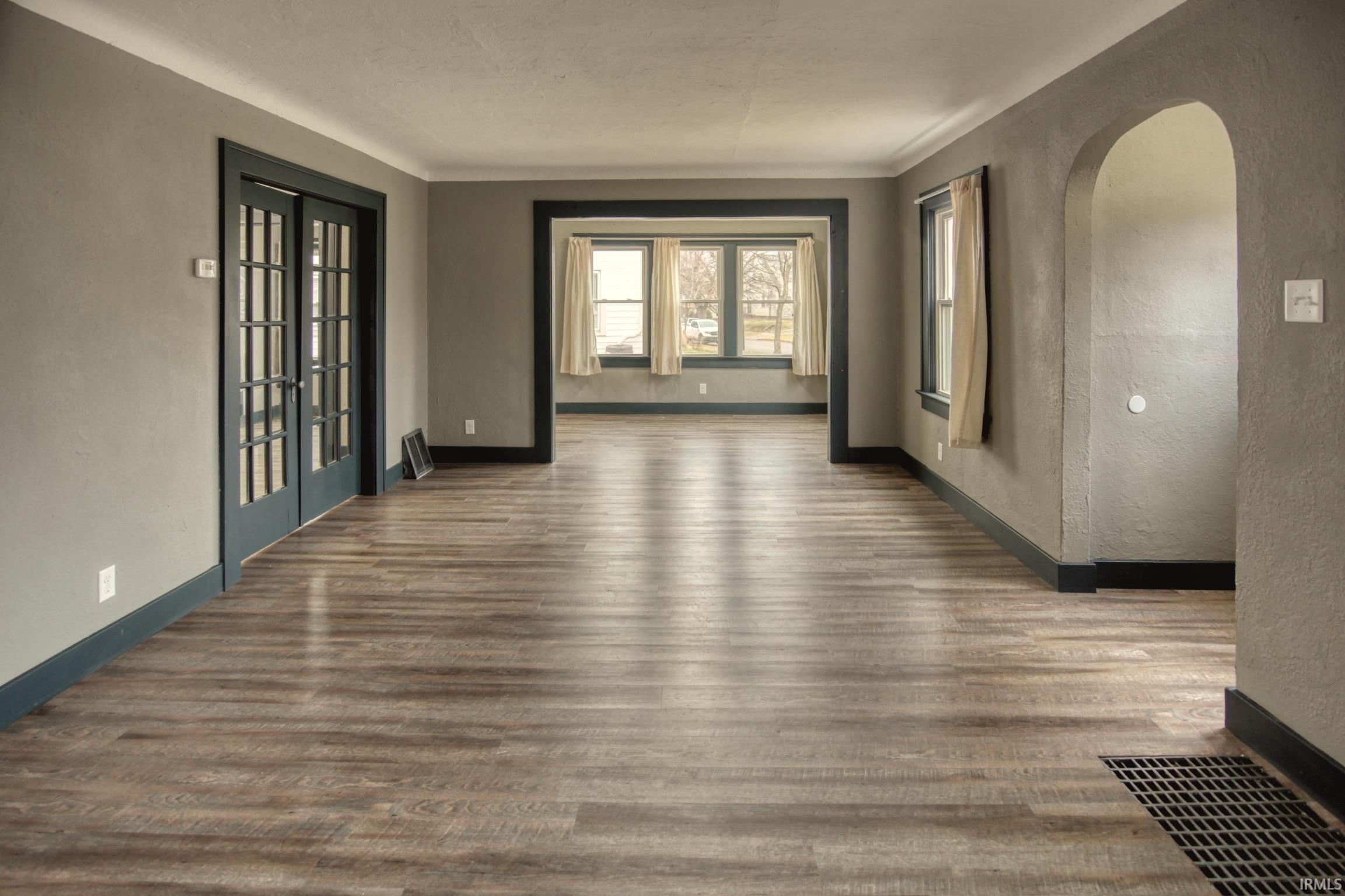 Empty room featuring arched walkways, a textured wall, wood finished floors, and french doors