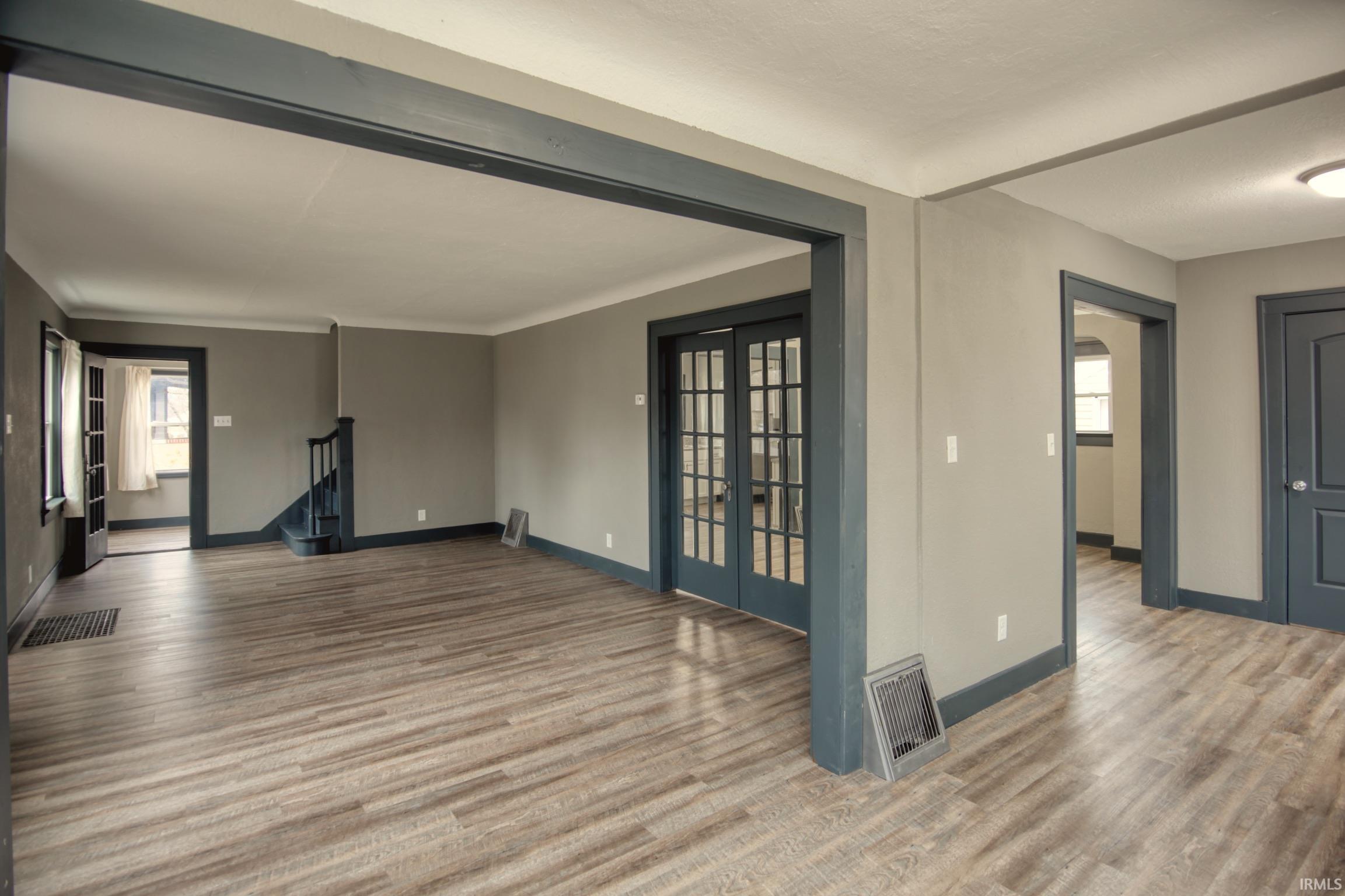 Unfurnished living room with french doors, wood finished floors, and stairs