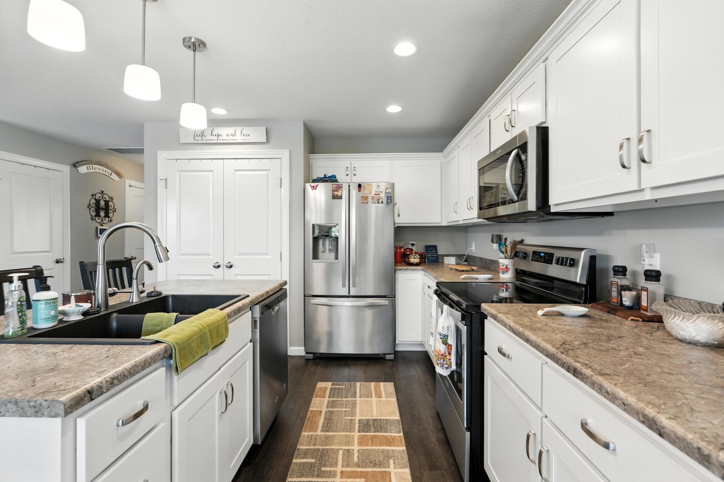 Kitchen with stainless steel appliances, white cabinetry, decorative light fixtures, dark wood-style flooring, and a kitchen island with sink