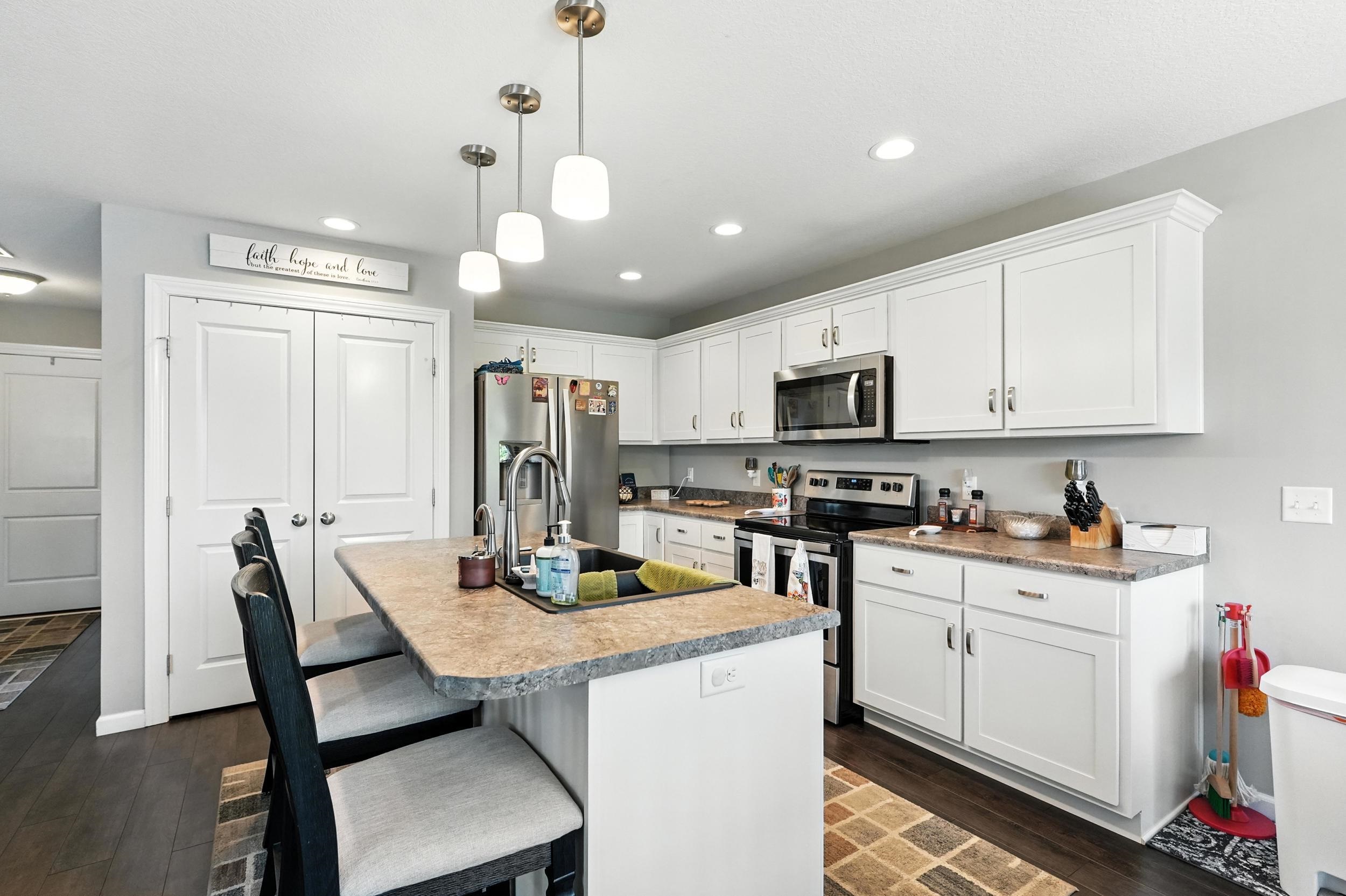 Kitchen with stainless steel appliances, white cabinets, light countertops, pendant lighting, and an island with sink