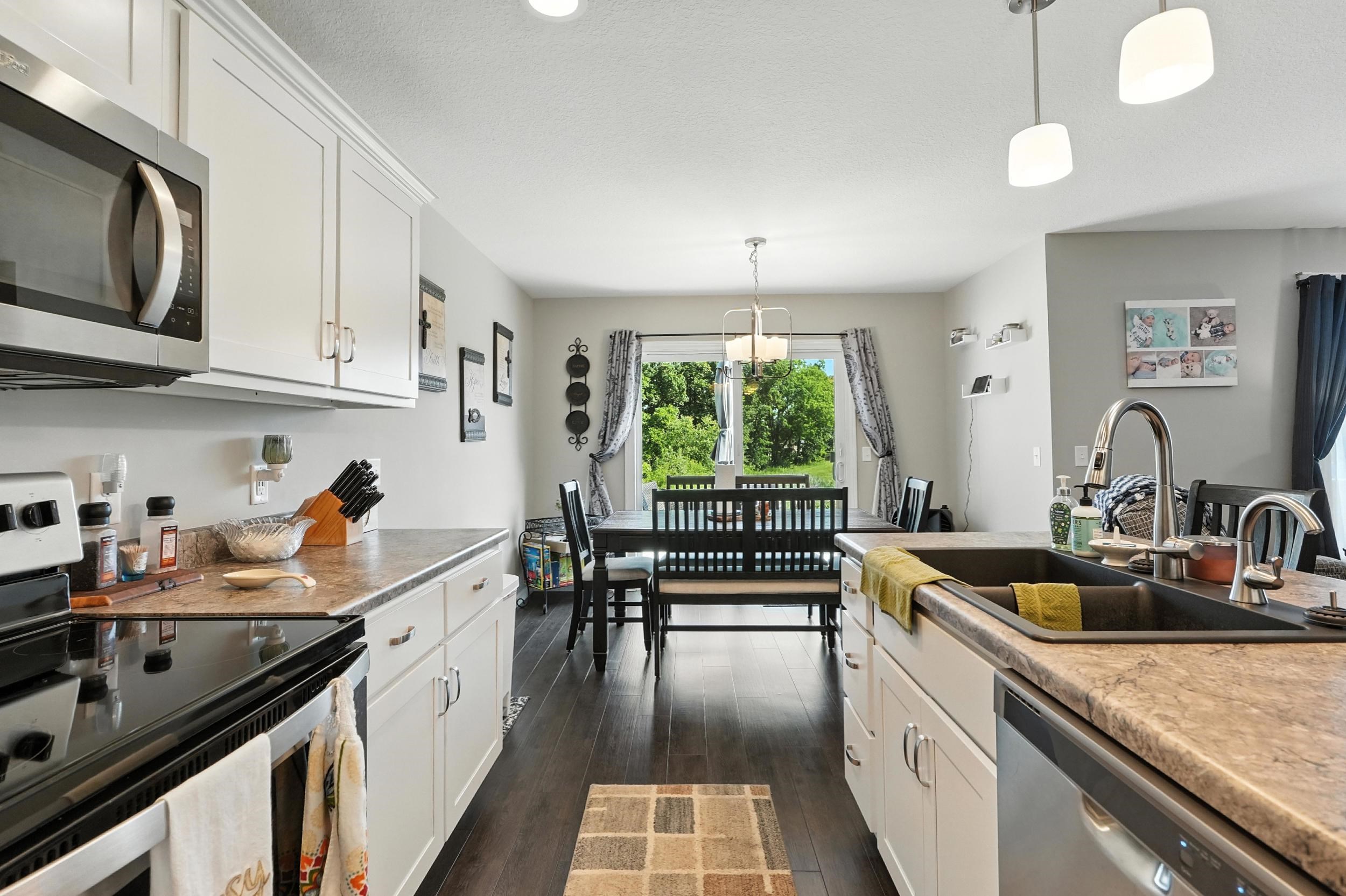 Kitchen featuring stainless steel appliances, white cabinetry, pendant lighting, and dark wood-style flooring