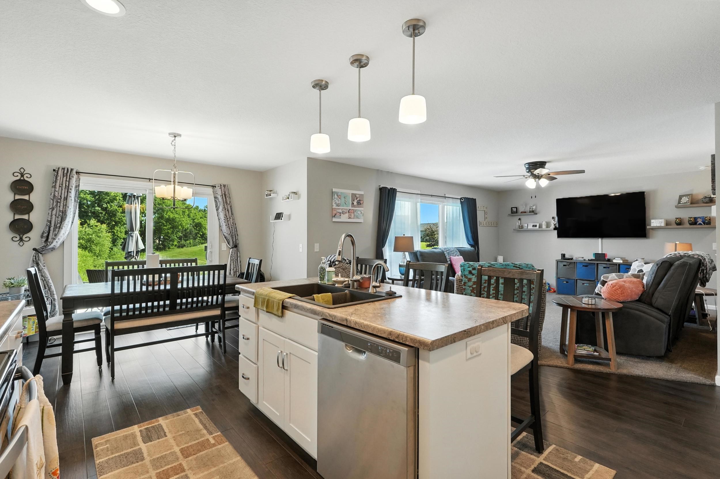 Kitchen with open floor plan, an island with sink, dishwasher, light countertops, and hanging light fixtures