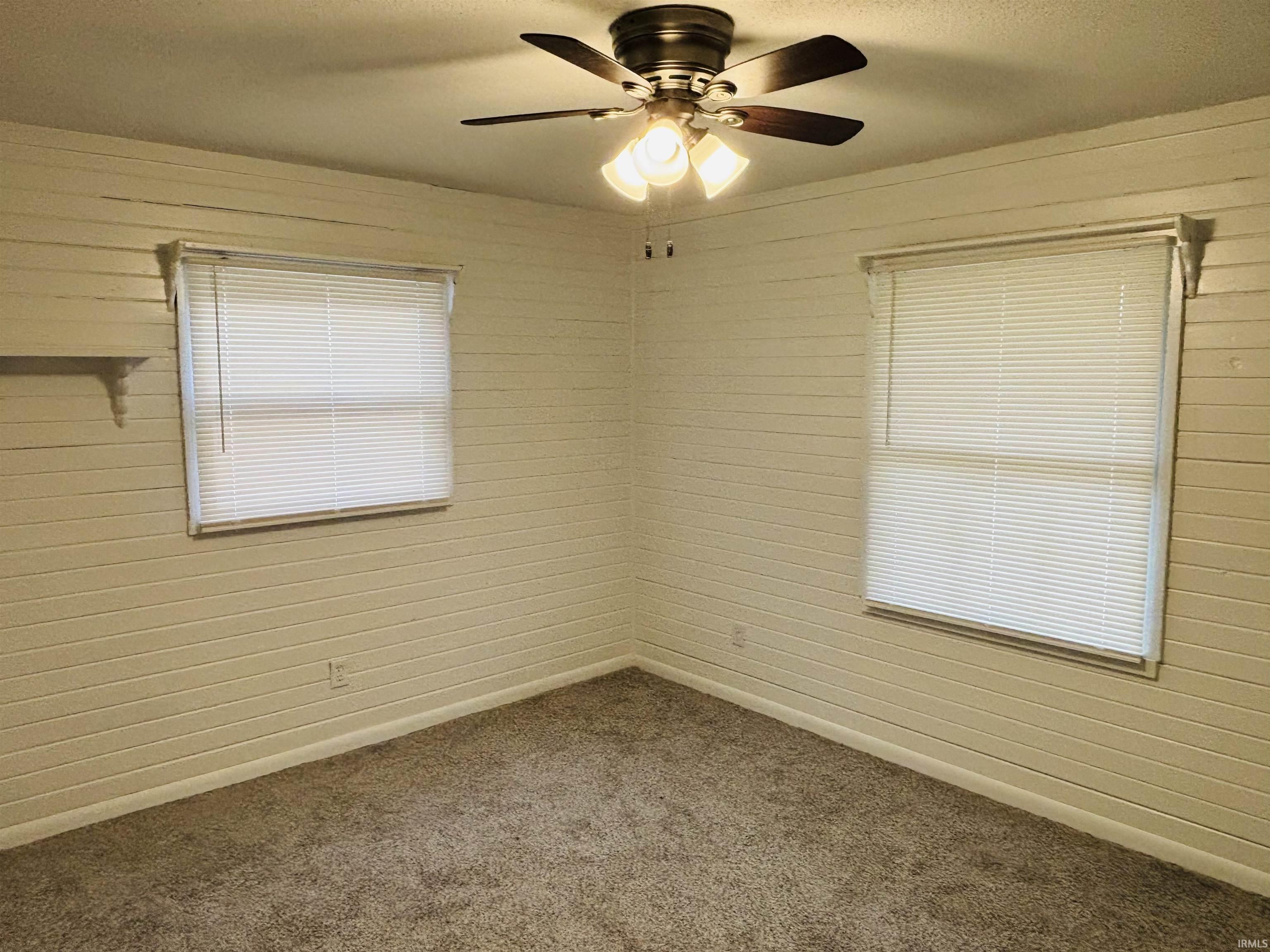 Spare room with a ceiling fan, dark carpet, and wooden walls
