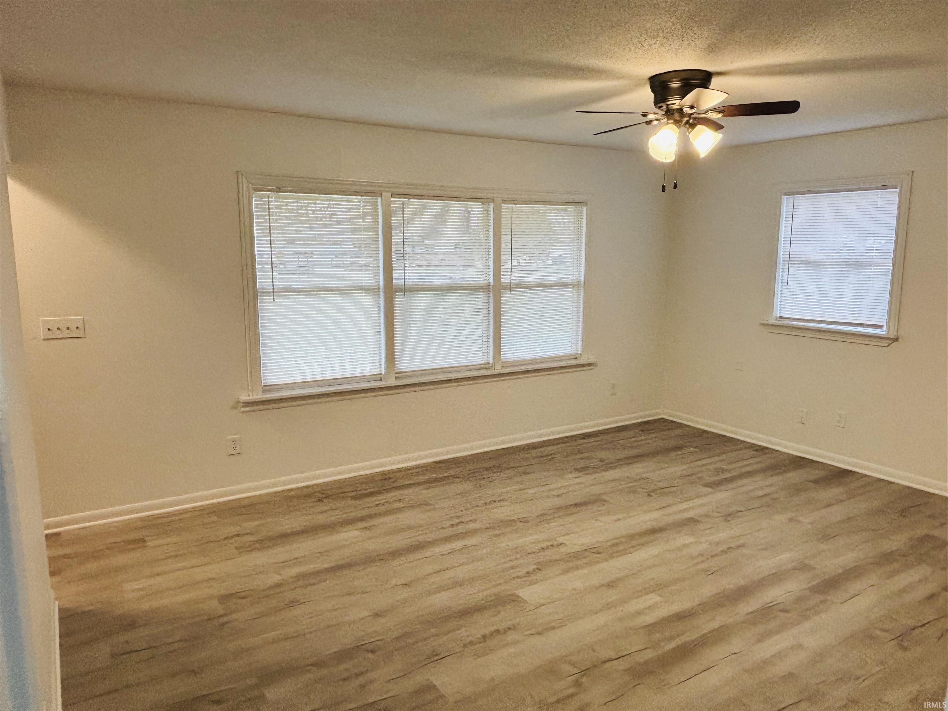 Empty room featuring wood finished floors, plenty of natural light, a textured ceiling, and ceiling fan