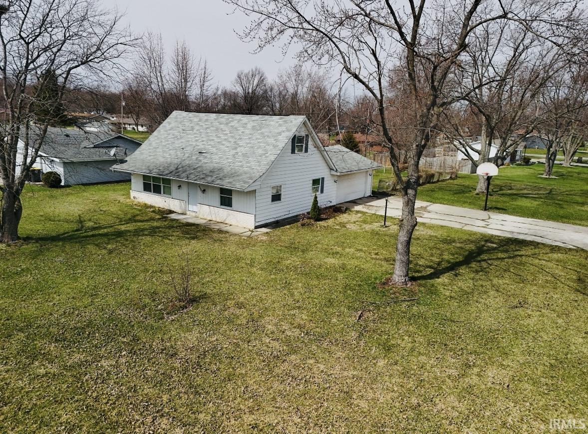 View of side of property with a yard, driveway, a shingled roof, and a garage