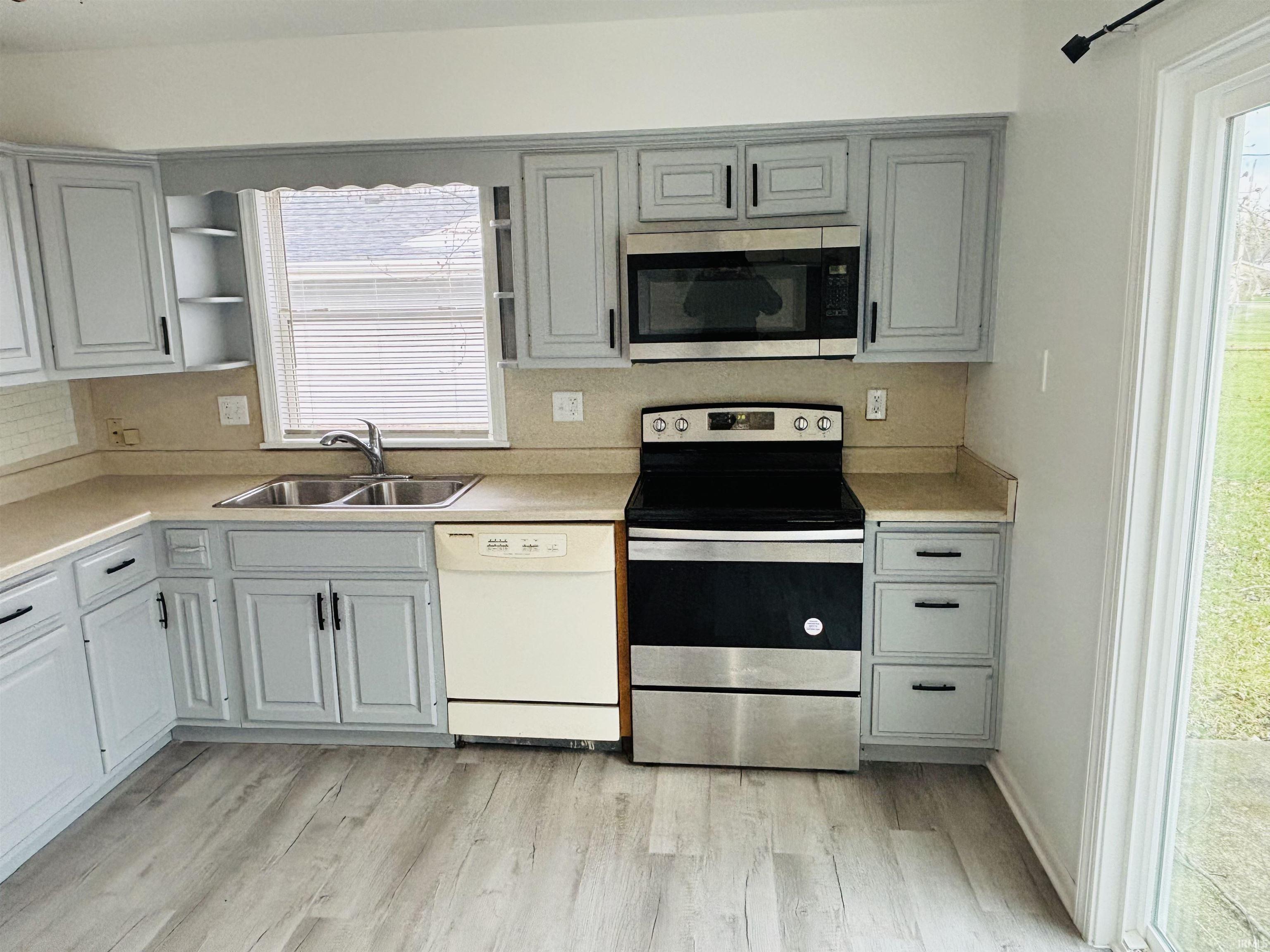 Kitchen with stainless steel appliances, light countertops, gray cabinetry, and light wood finished floors
