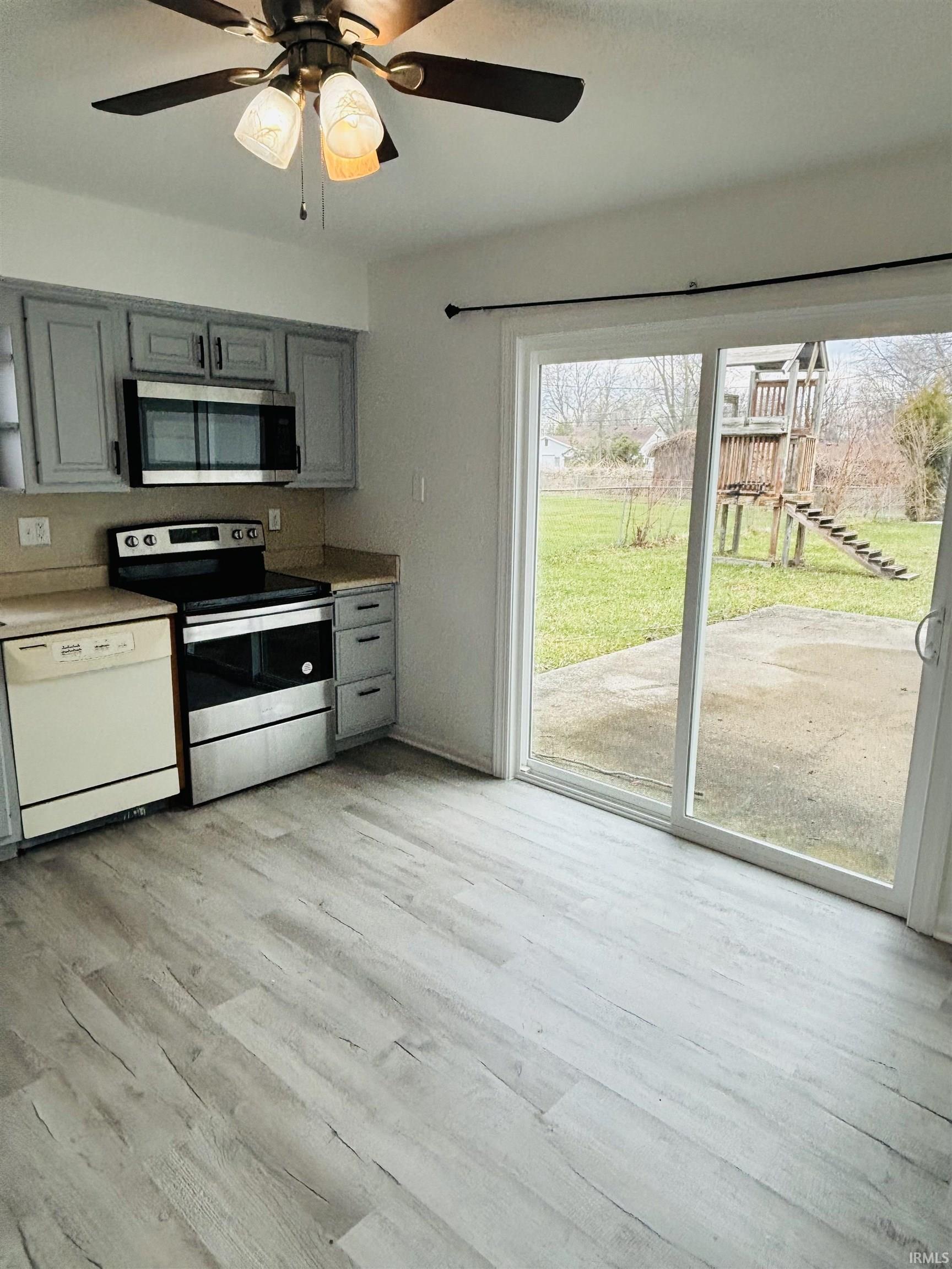 Kitchen featuring gray cabinetry, stainless steel appliances, ceiling fan, light wood finished floors, and light countertops