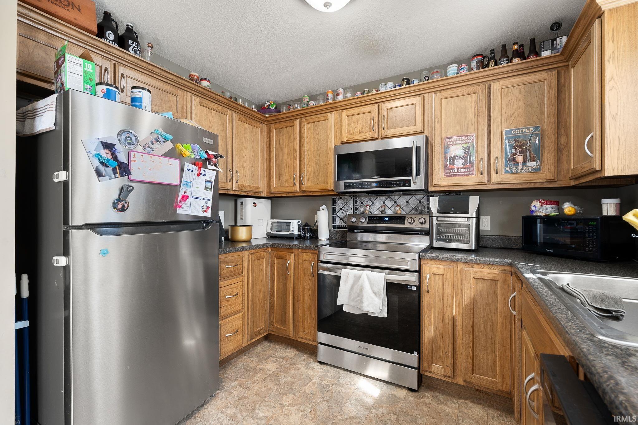 Kitchen featuring stainless steel appliances, dark countertops, and wood finish cabinetry