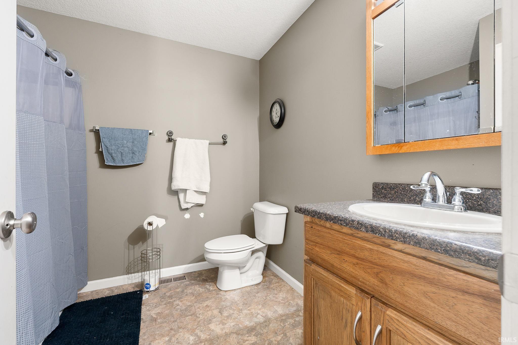 Full bath featuring vanity, a shower with curtain, stone finish flooring, and a textured ceiling