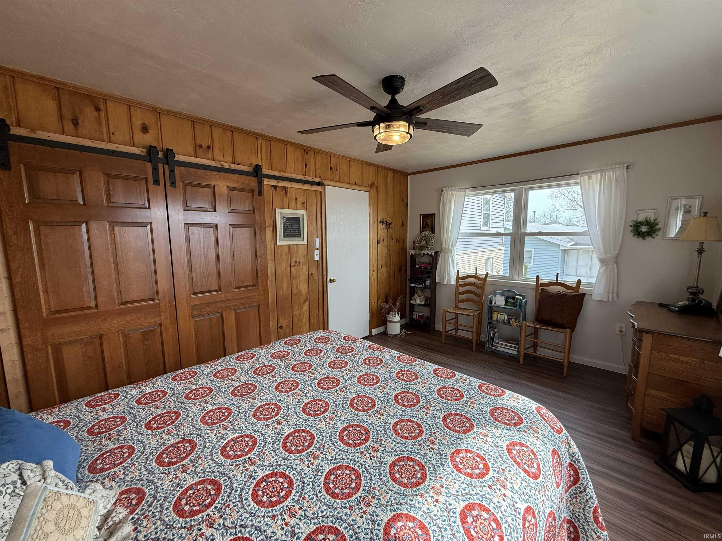 Bedroom featuring a barn door, dark wood finished floors, ceiling fan, a closet, and wood walls