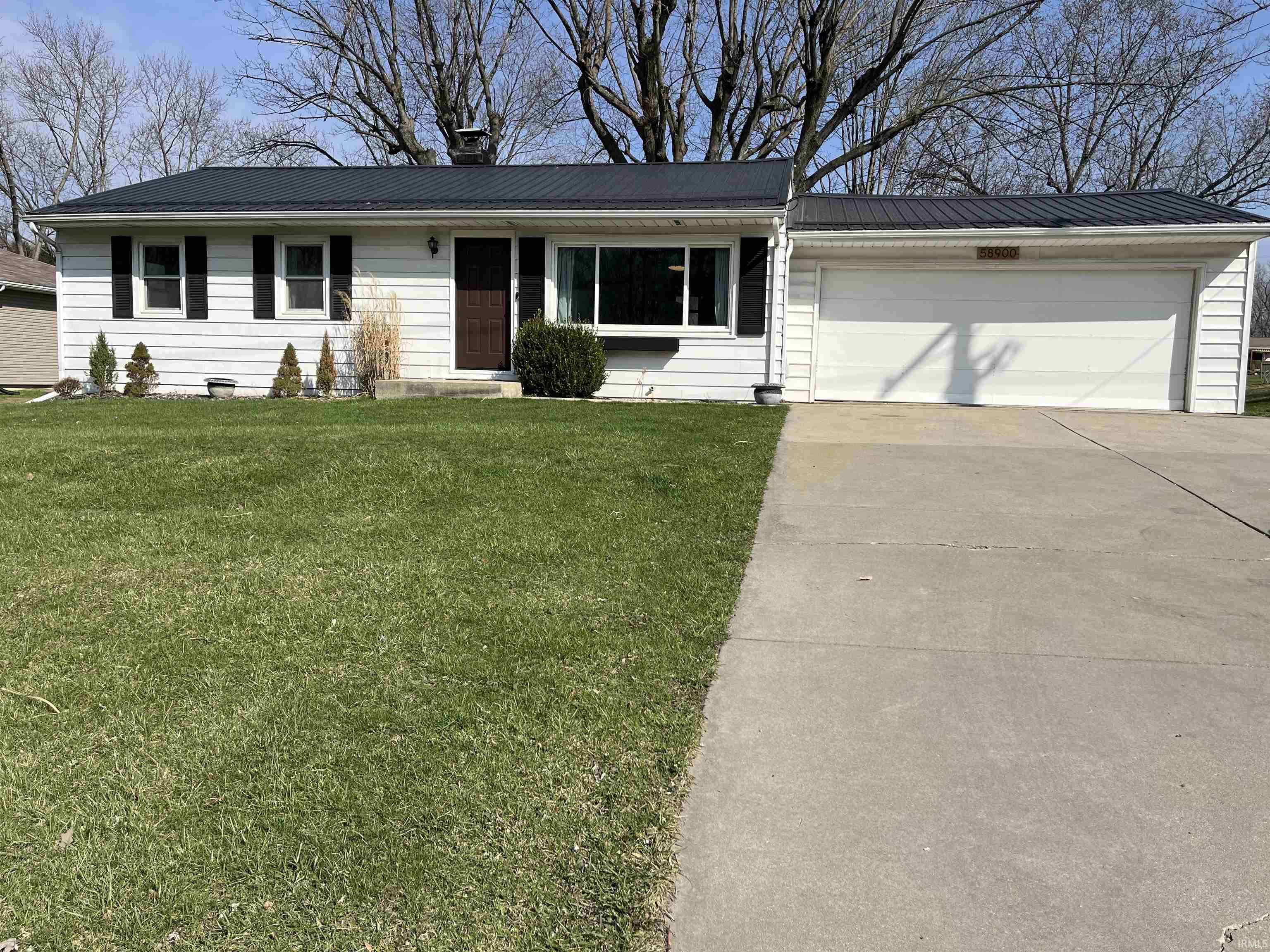 Ranch-style house featuring a front lawn, an attached garage, concrete driveway, and a chimney