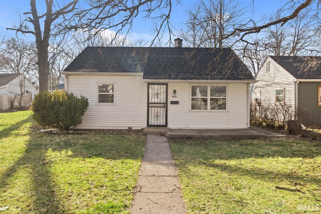 View of front facade featuring a front lawn, roof with shingles, and a chimney