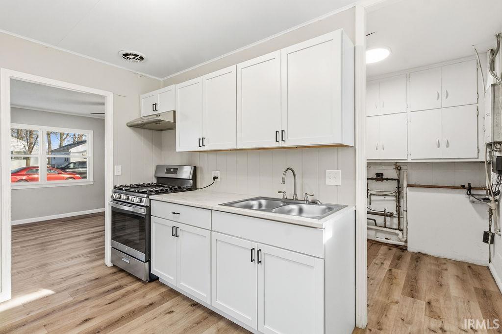 Kitchen featuring stainless steel range with gas stovetop, white cabinetry, light countertops, light wood-style flooring, and ornamental molding