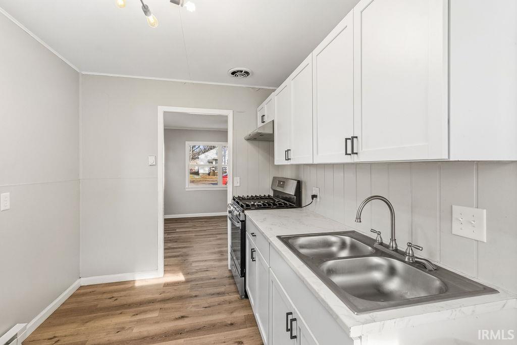 Kitchen featuring stainless steel gas stove, white cabinets, light countertops, light wood-style flooring, and baseboard heating
