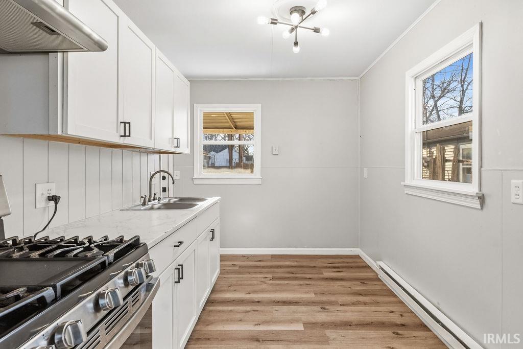 Kitchen featuring stainless steel gas range oven, white cabinetry, baseboard heating, and light wood-style flooring