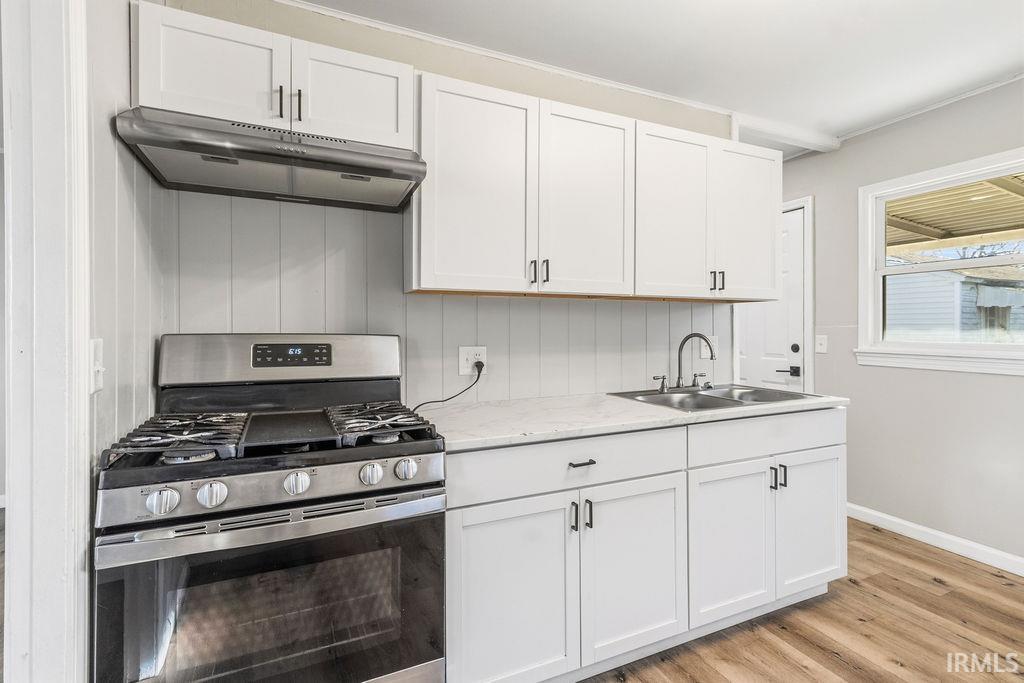 Kitchen with stainless steel range with gas stovetop, light countertops, white cabinets, and light wood-style flooring