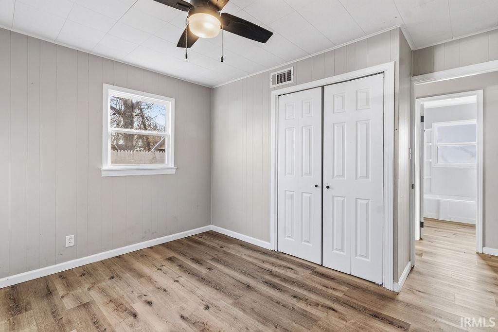 Unfurnished bedroom featuring a closet, light wood finished floors, ceiling fan, and wood walls