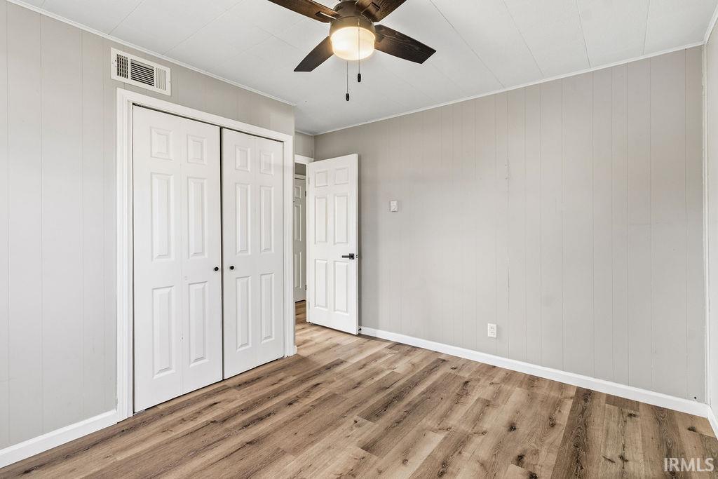 Unfurnished bedroom featuring wooden walls, light wood-style floors, a closet, ornamental molding, and a ceiling fan