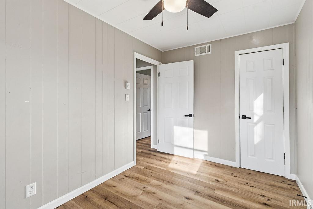 Unfurnished bedroom with light wood-style floors, ceiling fan, and wooden walls