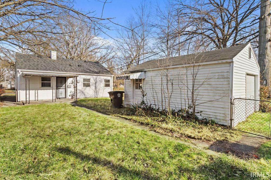 Rear view of house with a patio area, an outbuilding, a chimney, a garage, and roof with shingles