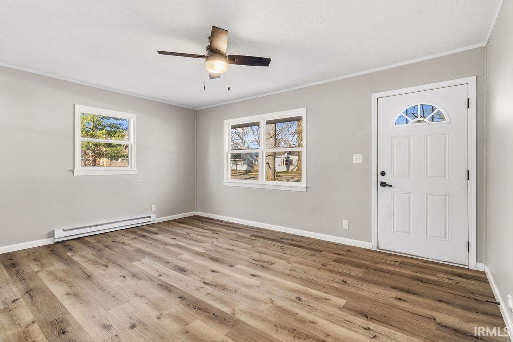 Foyer with a baseboard radiator, ornamental molding, a ceiling fan, and light wood-style flooring