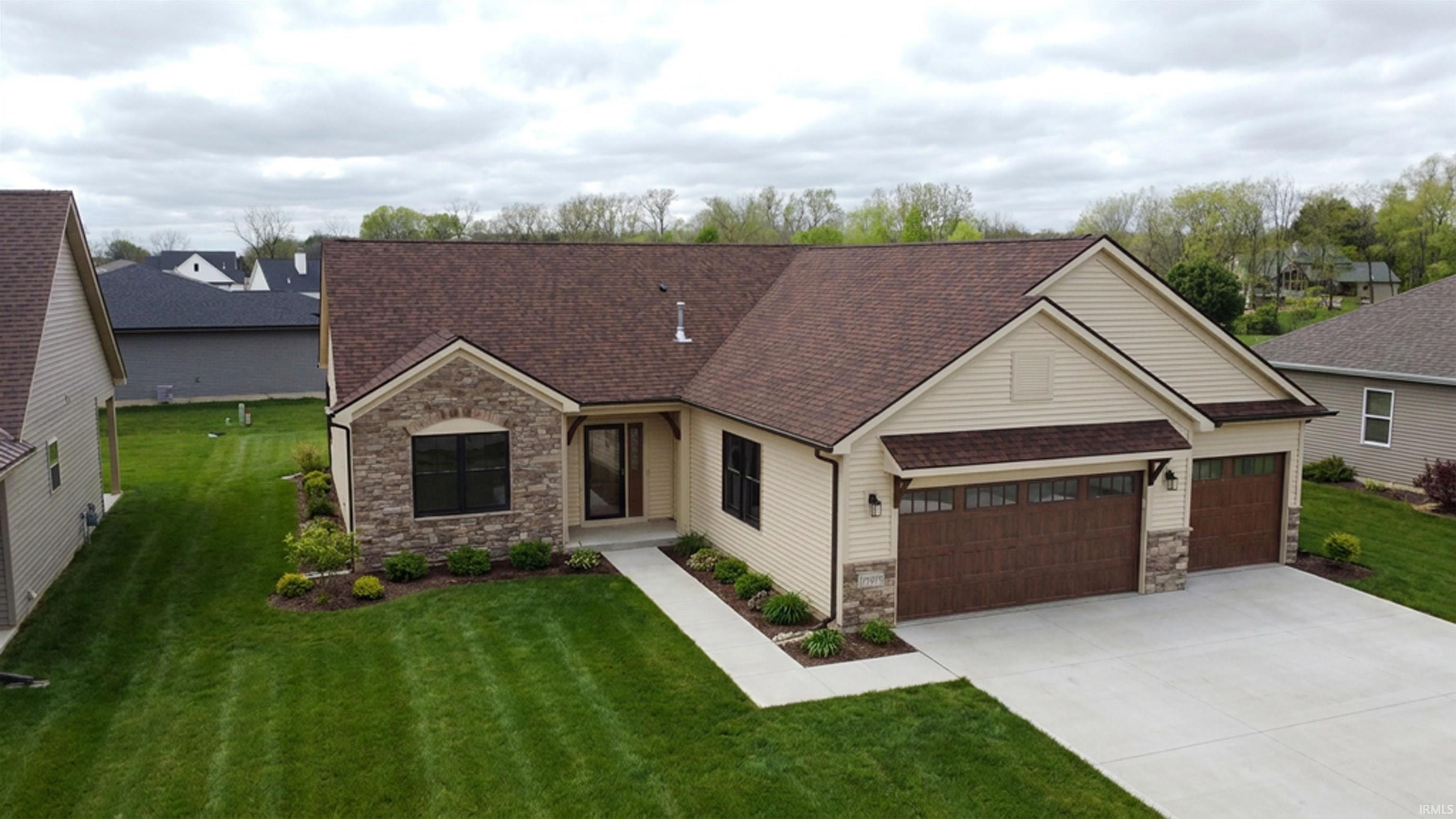 Contemporary residence featuring a stone and siding exterior, a two-car garage with wood-finish doors, a concrete driveway, a manicured front lawn, and mature landscaping