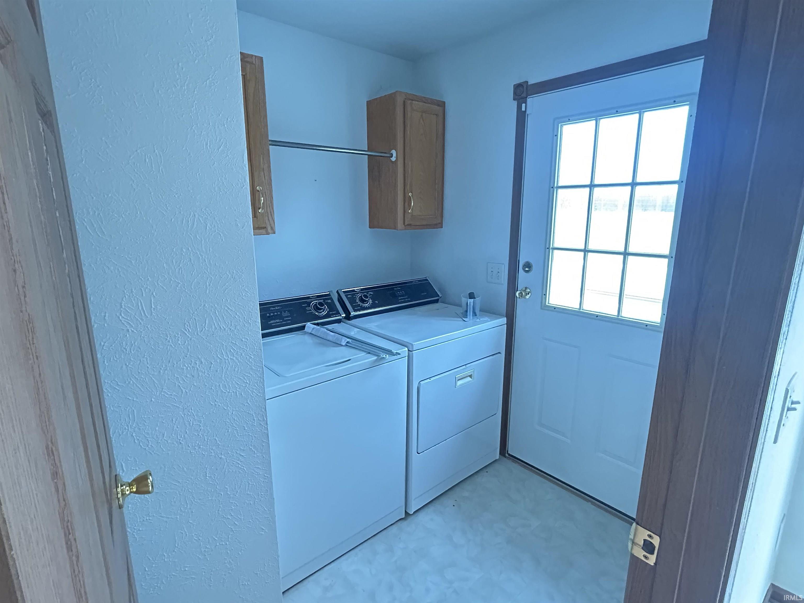 Laundry area featuring cabinet space, washing machine and dryer, light flooring, and a textured wall