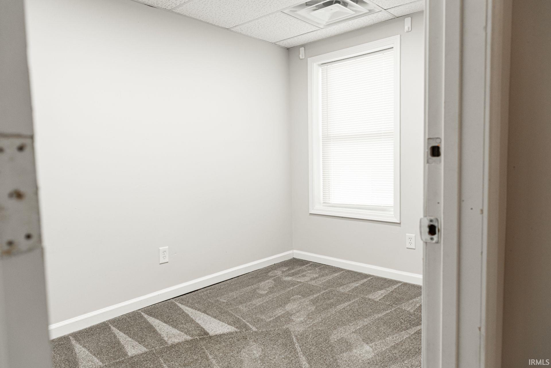 Unfurnished room with a drop ceiling and dark colored carpet