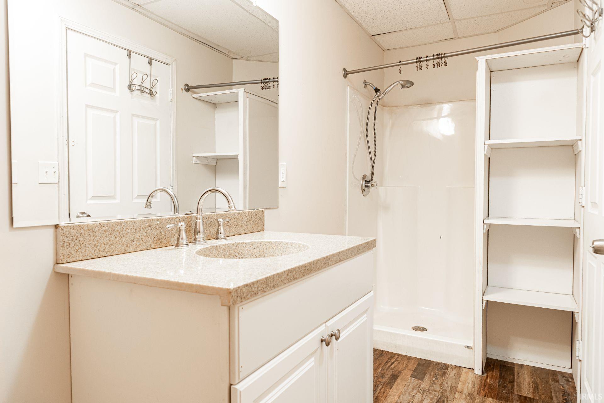 Bathroom featuring vanity, a stall shower, a drop ceiling, and light wood-type flooring