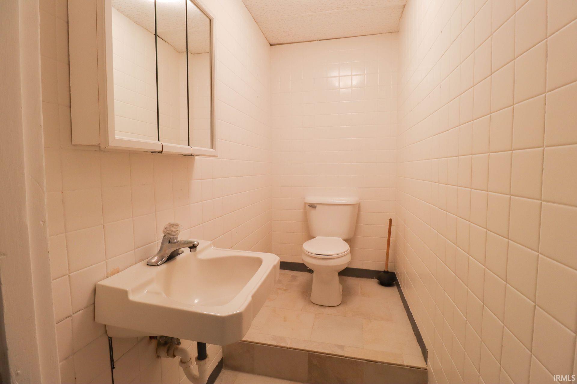 Half bathroom with toilet and tile walls