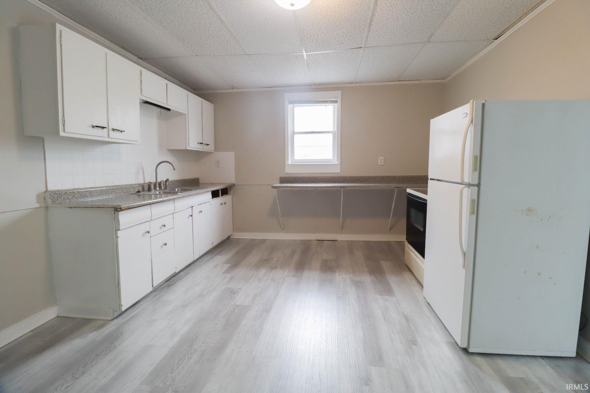 Kitchen featuring freestanding refrigerator, white cabinets, light countertops, light wood-style flooring, and range with electric cooktop